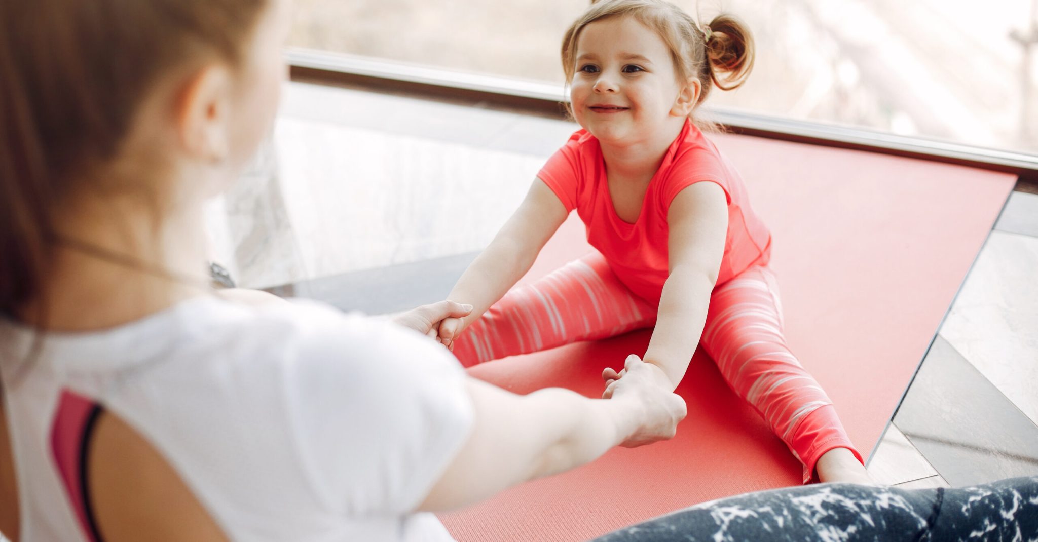 Woman in a sportswear. Mother with little daughter. Family are engaged in gymnastics in a gym